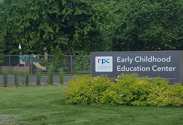 A brown early childhood center sign with a playground in the background. Very leafy and green.
