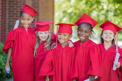 Diverse group of preschoolers wearing red graduation cap and gowns