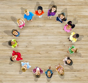 Diverse children in a circle looking up at camera (photo taken from above)