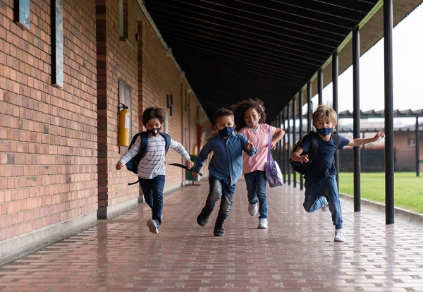 Kids running along covered school path wearing masks