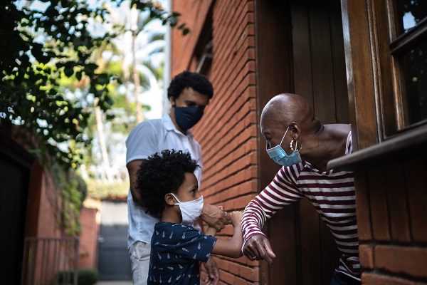Boy and father elbow-bumbing an older neighbor at her front door